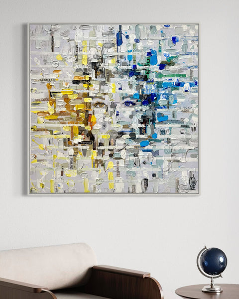 “Frontal view of MIND I by Marjolein Marx in an interior setting, with layered collage textures in blue, yellow, and grey forming a fragmented face. Displayed above a modern chair and globe, the piece invites contemplation through a balance of structure and emotion.”