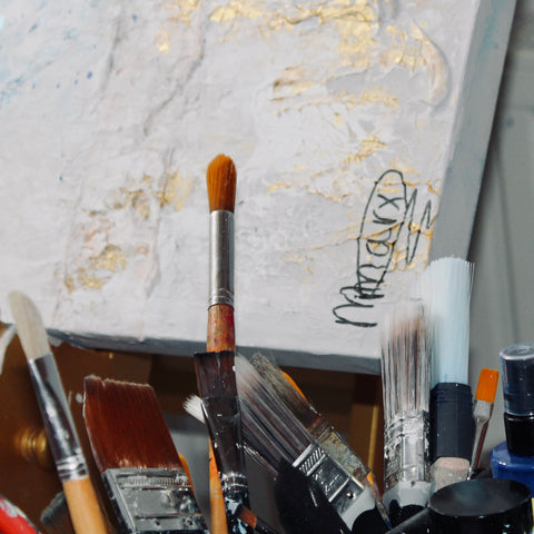 Bottom right detail of SOUL II by Marjolein Marx, showing a cluster of studio paintbrushes with the artist’s signature in the background on a textured and gold-accented canvas.